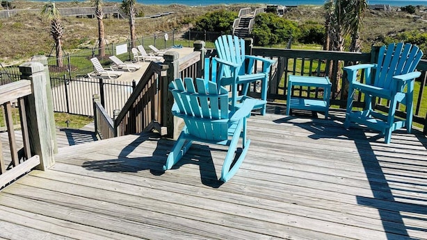 En träveranda med turkosa Adirondack-stolar och utsikt över havet.