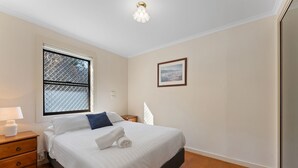 A hotel room with a bed, a nightstand, a lamp, a window with a metal screen, and a painting on the wall. - Shoal Bay Avenue 2 close to Beach (Shoal Bay)