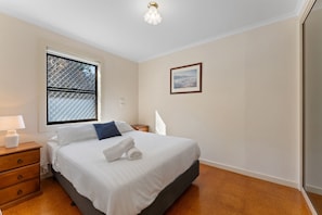 A hotel room with a bed, a nightstand, a lamp, a window with a metal screen, and a painting on the wall. - Shoal Bay Avenue 2 close to Beach (Shoal Bay)