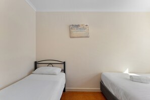 Una stanza piccola con due letti singoli, un quadro appeso al muro e una parete spoglia.