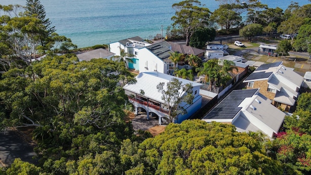 Zona residencial con casas, algunas con paneles solares, rodeada de abundante vegetación y vista al mar.