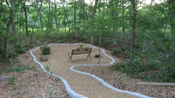 A park with a winding gravel path, a bench, and a metal fence.