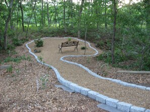 Ein Park mit einem gewundenen Kiesweg, einer Bank und einem Metallzaun.