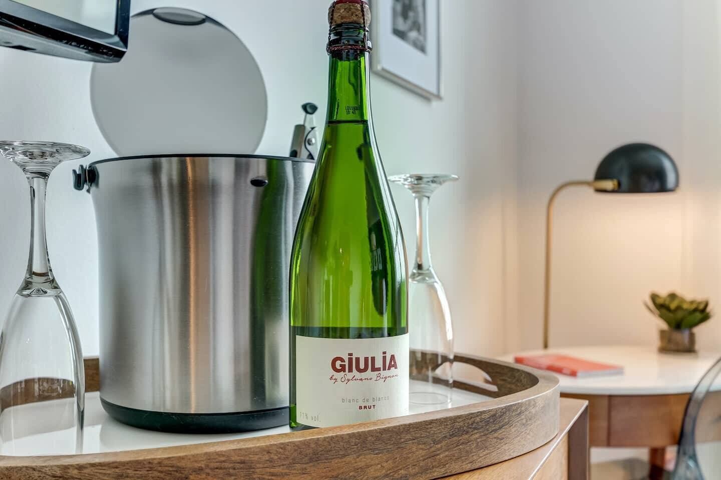 A bottle of Giulia wine on a tray with a stainless steel pot and wine glasses.