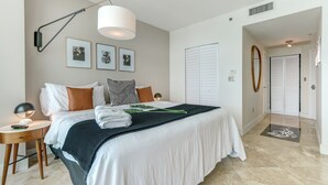 Une chambre bien rangée, avec un lit, une table de chevet, une lampe et des tableaux encadrés accrochés au mur.