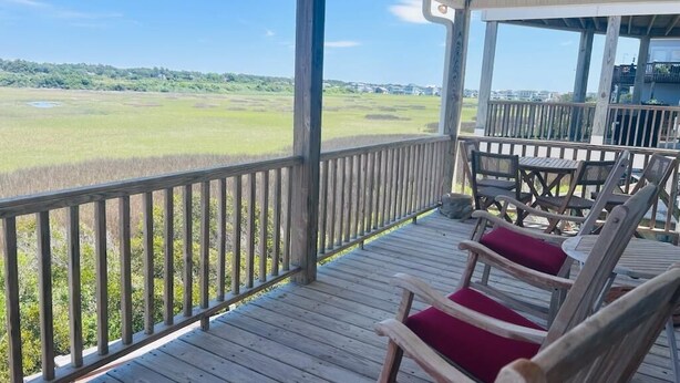 A covered outdoor area with wooden deck chairs and a view of a grassy field. - Libby's Lookout: Spacious 4-bedroom retreat near the beach in Holden Beach, NC. (Holden Beach)