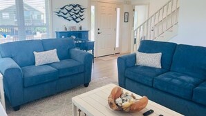 A living room with two blue sofas, a coffee table with decorative items, and a staircase. - Libby's Lookout: Spacious 4-bedroom retreat near the beach in Holden Beach, NC. (Holden Beach)