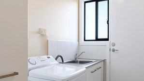 A compact laundry room with a front-loading washing machine, a sink, and a window above the door. - Blue Door Retreat  - Excellent Off Peak Special!  Nightly rates reduced!! (Edithburgh)