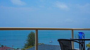 Un balcon avec vue sur la mer, une table avec un pichet bleu et une chaise.