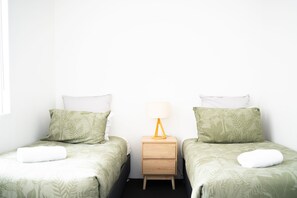 Ein Doppelzimmer mit zwei Betten, jedes mit einer grün gemusterten Bettdecke, einem Nachttisch mit Lampe und einer kleinen Schublade.