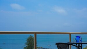 A balcony with a view of the sea, a table with a pitcher and glasses, and a chair. - Blue Waters Unit 8/59 Ronald Ave, Shoal Bay - This cosy unit has the views and the position! (Shoal Bay)