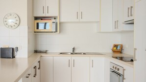 A modern kitchen with white cabinets, a microwave, a sink, and a toaster. - Blue Waters Unit 8/59 Ronald Ave, Shoal Bay - This cosy unit has the views and the position! (Shoal Bay)