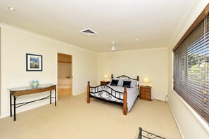 A bedroom with a bed, bedside lamps, a desk, a window with blinds, and a ceiling fan. - Marine Stunning Waterfront Home in Fingal Bay (Fingal Bay)