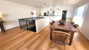 Un comedor amplio con mesa de madera y sillas de mimbre, una cocina al fondo y una escalera con barandilla negra.