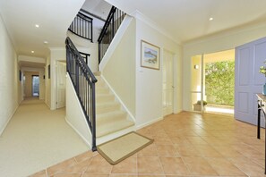 A spacious hallway with a carpeted staircase, a framed picture on the wall, and a door leading to an outdoor area. - Marine Stunning Waterfront Home in Fingal Bay (Fingal Bay)