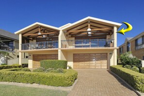 A two-story residential building with a balcony, a garage, and a paved driveway. - Marine Stunning Waterfront Home in Fingal Bay (Fingal Bay)