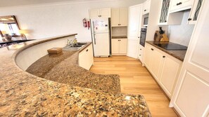 A kitchen with granite countertops, white cabinets, a refrigerator, and a microwave.