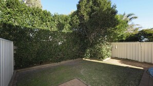 Un patio trasero con césped, un árbol alto y una cerca de metal.