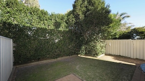 Un patio trasero con césped, un árbol alto y una cerca de metal.