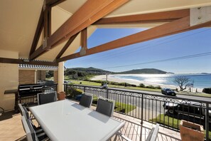 A balcony with a table and chairs, overlooking a beach and the sea. - Marine Stunning Waterfront Home in Fingal Bay (Fingal Bay)
