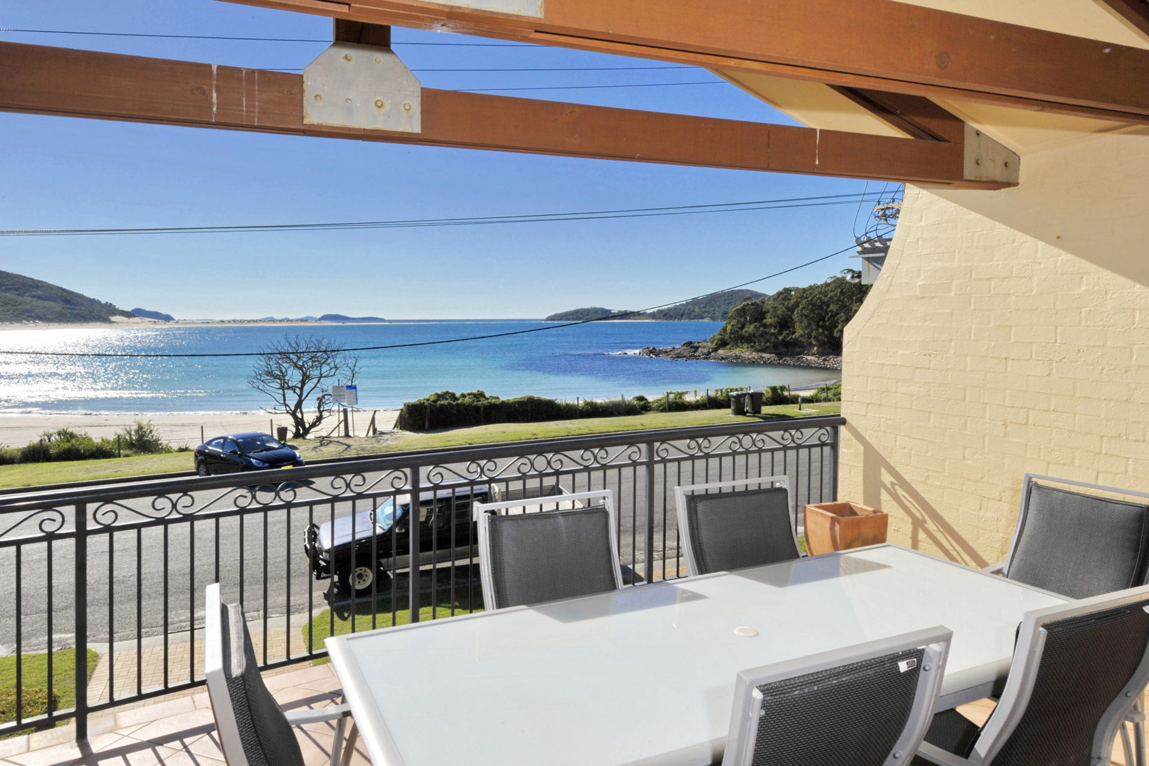 En balkon med et bord og stole, der vender ud mod en strand og havet.
