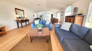 A spacious living room with a blue sofa, a wooden coffee table with a plant, and a kitchen in the background.