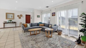 A modern living room with a grey sofa, two wooden side tables, a patterned rug, and a large window with sheer curtains.