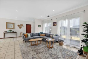 A modern living room with a grey sofa, two wooden side tables, a patterned rug, and a large window with sheer curtains.