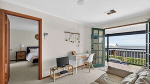 A spacious living room with a balcony, a desk, a television, and a comfortable sofa.