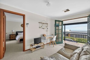 A spacious living room with a balcony, a desk, a television, and a comfortable sofa.