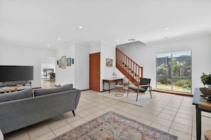 A spacious living room with a grey sofa, a TV, and a staircase leading to another level.