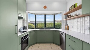 A modern kitchen with green cabinets, a built-in oven, and a large window offering a view of greenery.