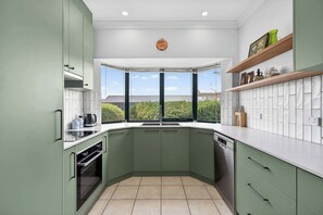 A modern kitchen with green cabinets, a built-in oven, and a large window offering a view of greenery.