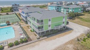 A multi-story building with a pool, tennis court, and beach view. - Relax and unwind in Feelin' Beachy (Holden Beach)