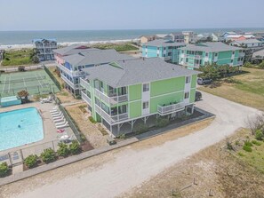 A multi-story building with a pool, tennis court, and beach view.