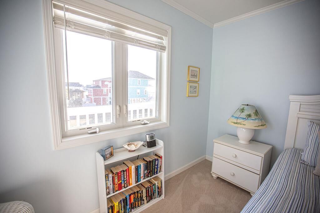 A bedroom with a large window, a bookshelf, a nightstand, and a bed.