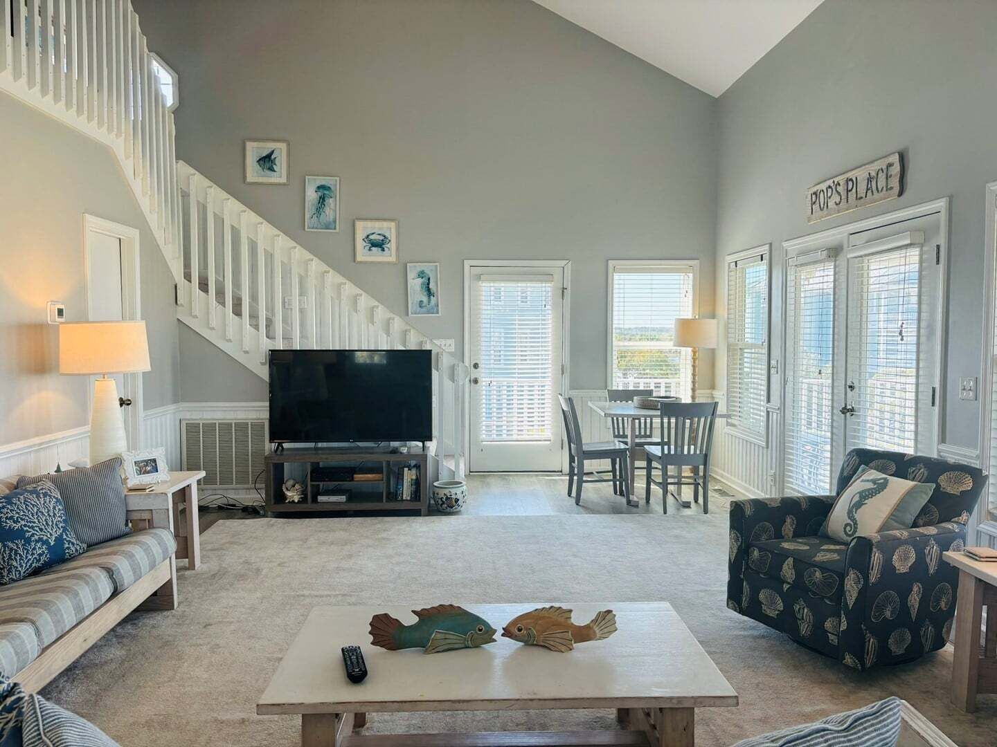 A living room with a TV, a staircase, a dining area, and a sign that says 'POP'S PLACE'.