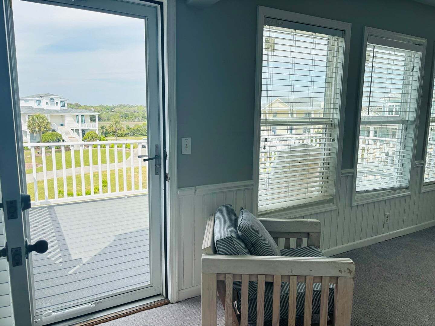 Una habitación con puerta corrediza de vidrio que da a un balcón, un banco con cojines y tres ventanas con persianas.