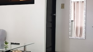 Una habitación moderna con una mesa de centro de vidrio, un cuadro en la pared, una puerta con espejo y suelo de baldosas.