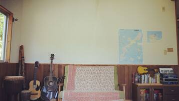 A room with a wooden bench, a guitar, a tambourine, a drum, and a keyboard. There are maps on the wall and a cabinet with books and a suitcase.