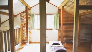 Una baita con camera da letto a soppalco, pareti in legno, una finestra con tende e un letto con cuscini.