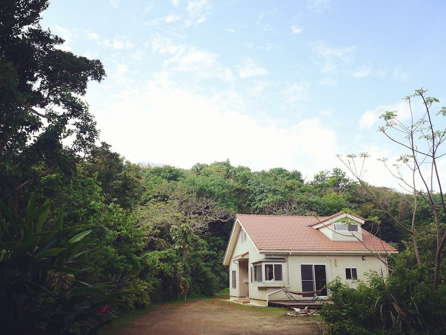 Uma casa térrea com telhado de telhas vermelhas, rodeada por muita vegetação e árvores.