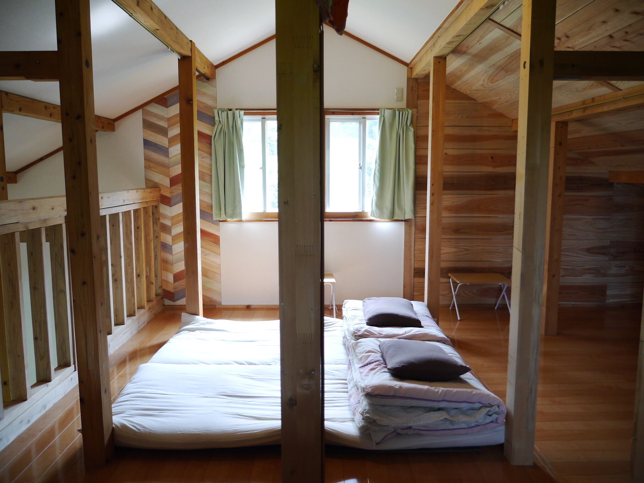 Een chalet met een slaapkamer op een entresol, houten wanden, een raam met gordijnen, en een bed met kussens.