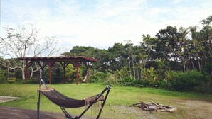 Un'amaca su un pontile di legno, un gazebo in legno e una zona erbosa con alberi sullo sfondo.