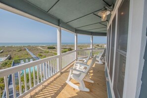 A covered porch with white rocking chairs, a wooden deck, and a view of the beach and ocean. - Oceanfront oasis in Holden Beach! Spacious 6BR, 6BA, sleeps 14. (Holden Beach)