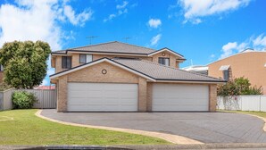 A two-story house with a garage, a well-maintained lawn, and a clear blue sky. - Fingal Sands 10A - Fingal Bay (Fingal Bay)