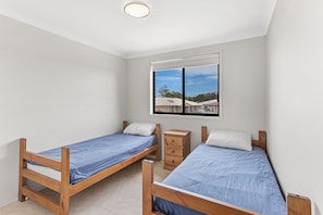 A bedroom with two wooden beds, a nightstand, and a window with a view of buildings.