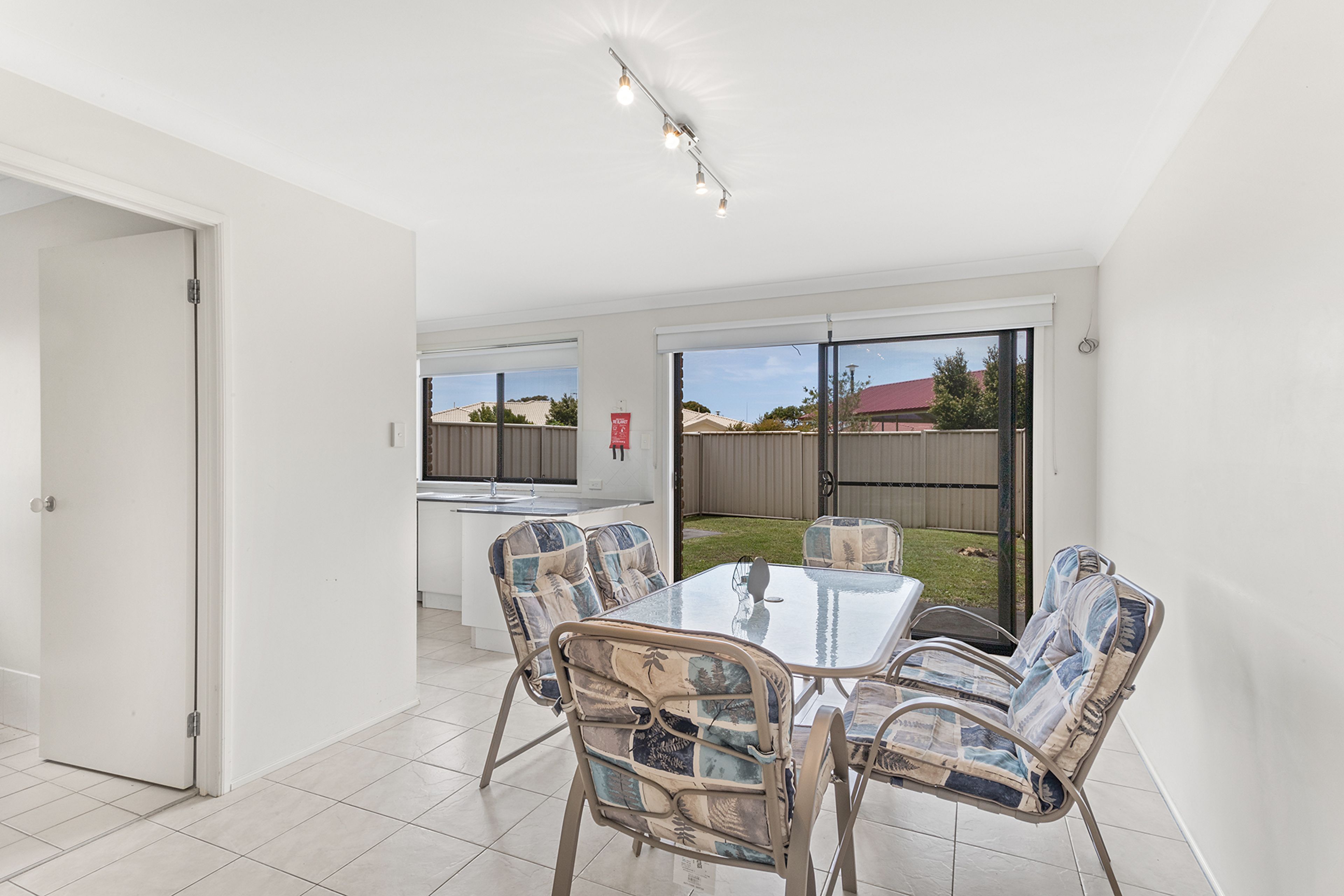 A dining area with a table and chairs, a kitchen in the background, and a view of the backyard through glass doors.