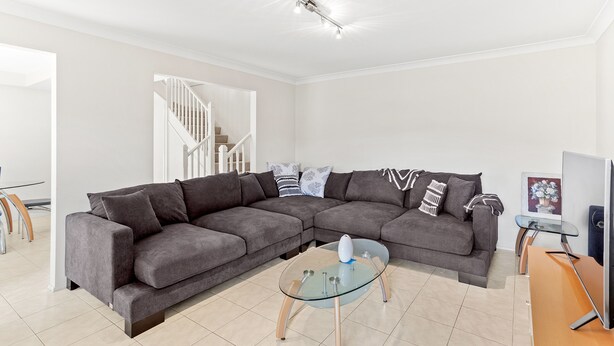 A modern living room with a sectional sofa, a glass coffee table, and a staircase leading to another level. - Fingal Sands 10A - Fingal Bay (Fingal Bay)
