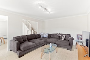 A modern living room with a sectional sofa, a glass coffee table, and a staircase leading to another level.